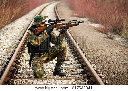 The soldier or hunter in military uniform is aiming with cross-bow on railway outdoors in nature.