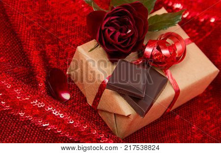 gift Packed in craftool paper with a dark red rose on shiny fabric and chocolate