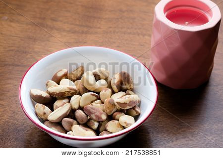 Bowl of brazil nuts next to a candle on a wooden table. Brazil nuts are rich in protein and selenium and are considered health foods for thyroid conditions.