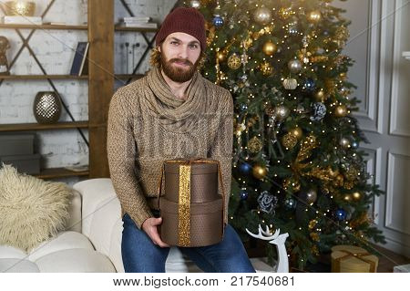 Guy smiles and keeps boxes with christmas gifts christmastree on baxkground holiday home concept