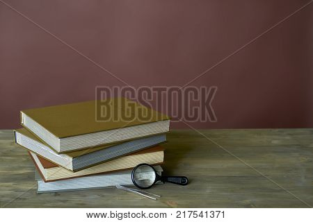 Four stamp albums books bunch, magnifier and tweezers on wooden table and bordeaux background
