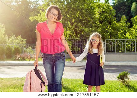 Mom and pupil of elementary school  holding hands. The parent takes the child to school. Outdoors, return to the concept of the school.