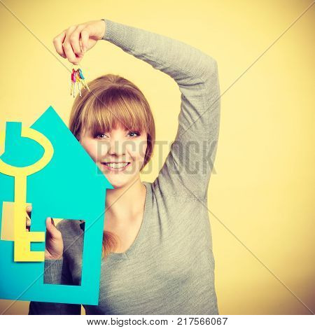 Ownership and property concept. Young blonde smiling female owner with bunch of colorful keys and house. Woman with key antry to her first own flat.