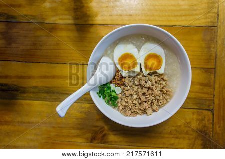 Minced pork congee with egg fresh ginger and coriander on white cup and spoon over the wood table.