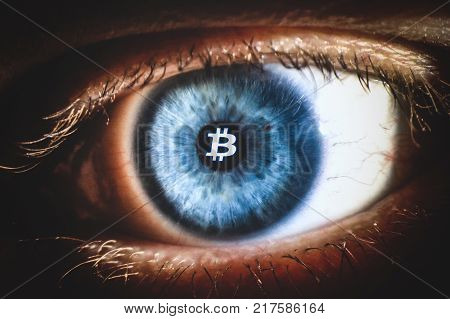 An enlarged image of eye with a blue iris, eyelashes and sclera. Bitcoin symbol inside the pupil. the shot is made by a slit lamp with integrated camera.