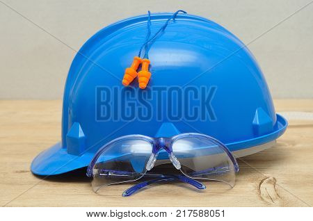 A hard hat safety glasses and a pair of ear plugs isolated on a wooden background