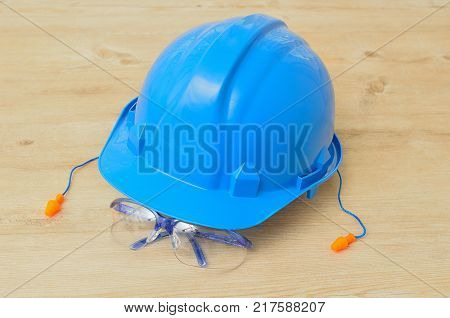 A hard hat safety glasses and a pair of ear plugs isolated on a wooden background
