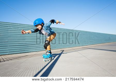 Side view portrait of preteen boy, roller skater in helmet and protective gear, skating fast at outdoor rollerdrom