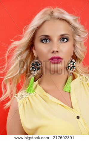 young beautiful girl in gren earrings on an red background