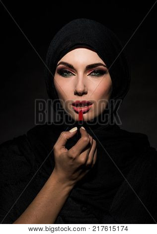Young beautiful muslim woman putting red lipstick