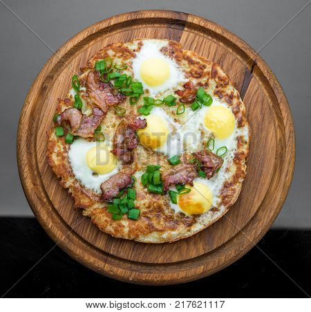 Plate with fried eggs, bacon, tomato and potato griddle cakes close up. Wooden background