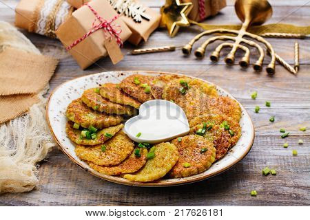 Traditional Hanukkah dish latkes - potato pancakes with sour cream. Table decorated with menorah, gift boxes and candles