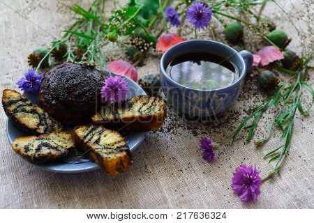 Sweet bun with flax seed and poppy and cup of tea on table.