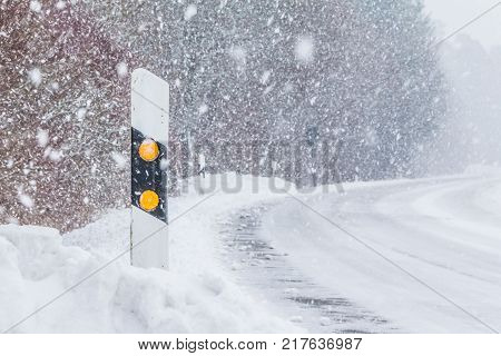 Reflector post at snowy slippery icy white snow winter road. The street track is slick and frozen. High dangerous risk of an accident through the blizzard snowstorm and severe weather at christmas time season.