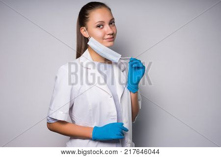 young smiling doctor girl in white medical dressing gown removes face mask from face