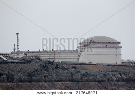 Large industrial oil refinery tank connected to massive storage unit and multiple metal pipes