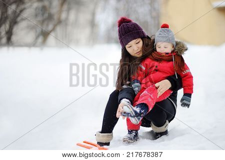 Young asian woman helping caucasian toddler boy with his winter clothing. Babysitting/childcarer concept.