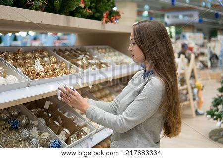 Beautiful happy customer girl choosing gifts for Christmas and New Year. She is taking Christmas tree decorations. Holiday shop