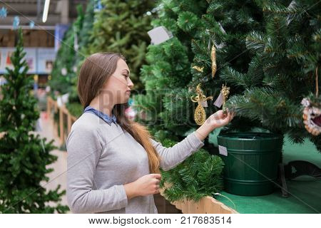 Cheerful happy customer girl choosing Christmas tree for the new year on Christmas Eve. difficult decision. Various choice