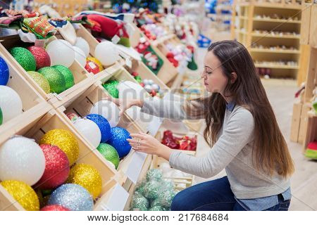 Cheerful happy customer girl choosing Christmas tree decoration balls. difficult decision. Various choice