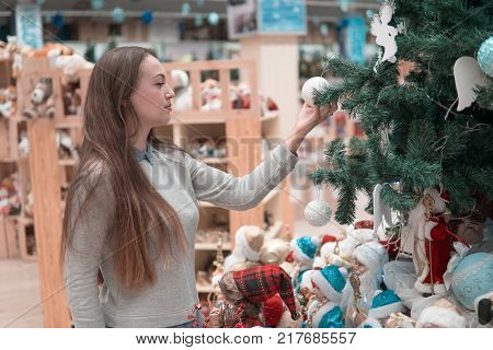 Cheerful happy customer girl choosing Christmas tree decorations for the new year on Christmas Eve. difficult decision. Various choice