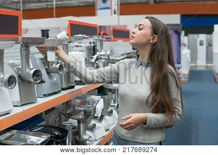 Smart female customer girl chooses meat grinder in a home appliance store. difficult decision. Various choice