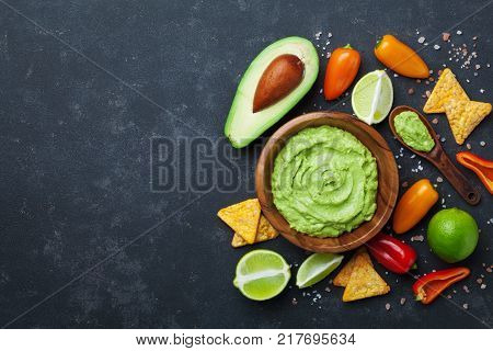 Traditional mexican food. Bowl guacamole sauce with avocado lime and nachos on black table top view. Copy space for recipe.
