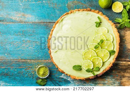 Key Lime Pie with several limes and mint over wooden background, top view with copy space.