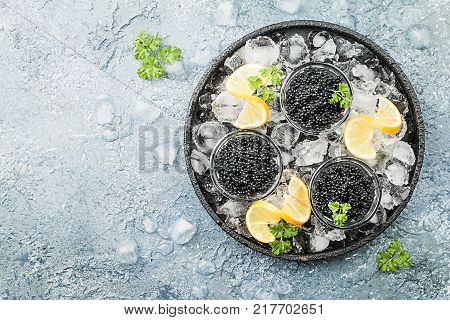 Black caviar in a glass bowl on ice with lemon close up over gray background, top view
