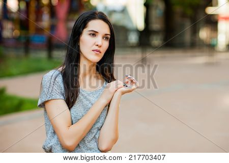 Young thoughtfull girl in gray shirt with long brunette hair in the street. Close up portrait