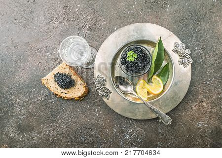 Black caviar in a glass bowl with lemon close up over dark background, top view
