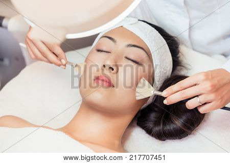 Close-up of the face of a beautiful young Asian woman relaxing during rejuvenating facial massage with brushes in a contemporary beauty center