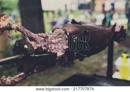 Lamb barbecue roasted at spit. Grill, big piece of meat at rolling skewer. Street vendor, professional chef hands cooking bbq food, unrecognizable. Catering concept
