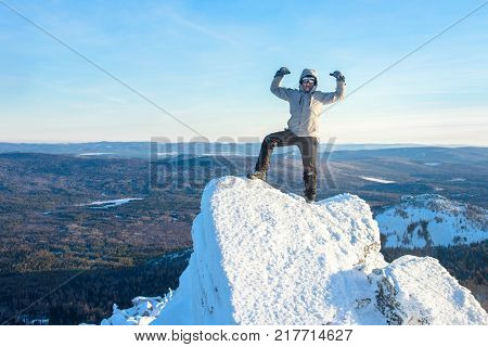 The mountaineer climbed the mountain top covered with ice and snow, man hiker standing at the peak of rock and celebrates the success. Winter season