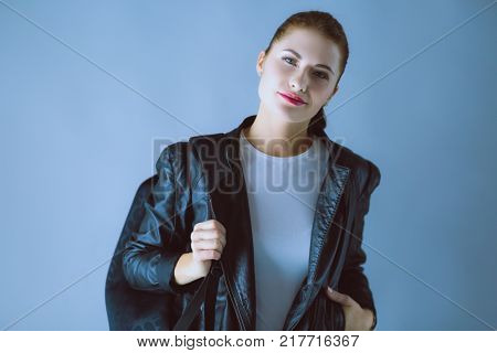 Portrait of beautiful young brunette woman in stylish black jacket on gray