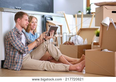 Young couple moving in new home.Sitting and relaxing after unpacking.Looking something on laptop. Young couple