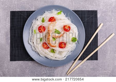 A top view on a chinese food. Chopsticks, shrimps and tomatoes on a rise nuddles on the marble background. Close-up of objects. Food concept.