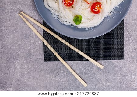 A top view on a chinese food. Chopsticks, shrimps and tomatoes on a rise nuddles on the marble background. Close-up of objects. Food concept.