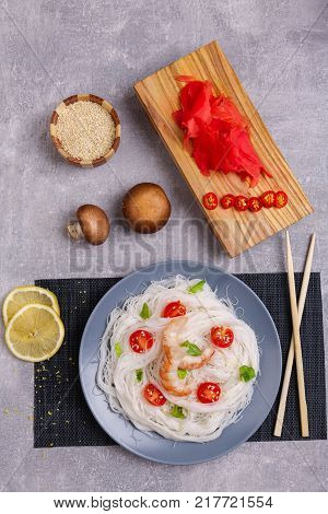 A top view on a chinese food. Chilli, chopsticks, shrimps mushrooms, slices of lemon and tomatoes on a rise nuddles on the marble background. Close-up of objects. Food concept.