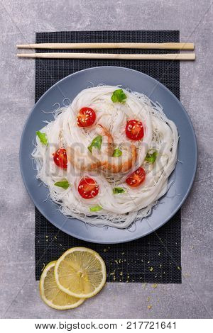 A top view on a chinese food. Chilli, chopsticks, shrimps and tomatoes and lemon on a rise nuddles on the marble background. Close-up of objects. Food concept.