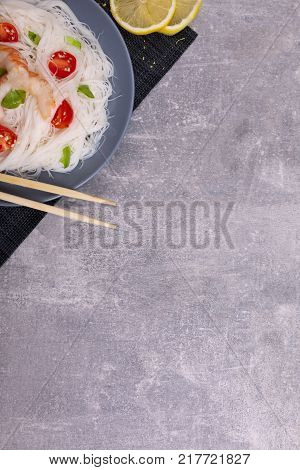 A top view on a chinese food. Chilli, chopsticks, shrimps and tomatoes and lemon on a rise nuddles on the marble background. Copy space. Close-up of objects. Food concept.