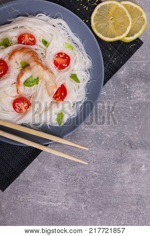A top view on a chinese food. Chilli, chopsticks, shrimps and tomatoes and lemon on a rise nuddles on the marble background. Close-up of objects. Food concept.