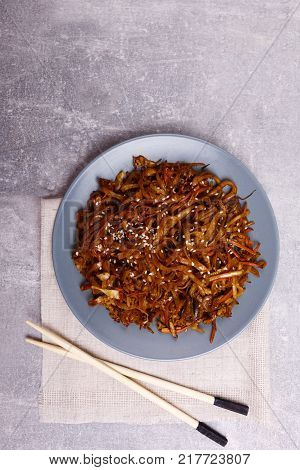 A top view on a chinese food. Chopsticks, Chinese spicy sea kale with chilli and mushrooms on the marble background. Close-up of objects. Food concept.