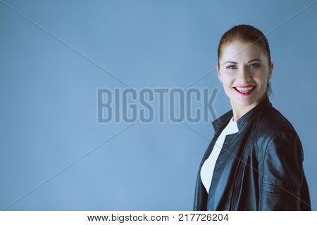 Portrait of beautiful young brunette woman in stylish black jacket on gray