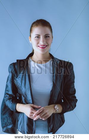 Portrait of beautiful young brunette woman in stylish black jacket on gray