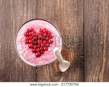 Idea for healthy breakfast on Valentine's Day: pink chia pudding with red berry puree and cranberries in shape of heart on top over wooden table background. Copy space for text Top view or flat-lay.
