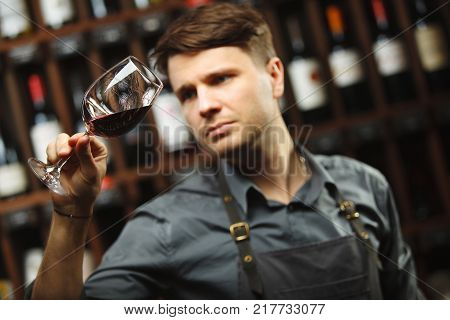 Bokal of red wine on background of male sommelier appreciating color, quality, flavor and sediments of drink. Professional degustation expert in winemaking.