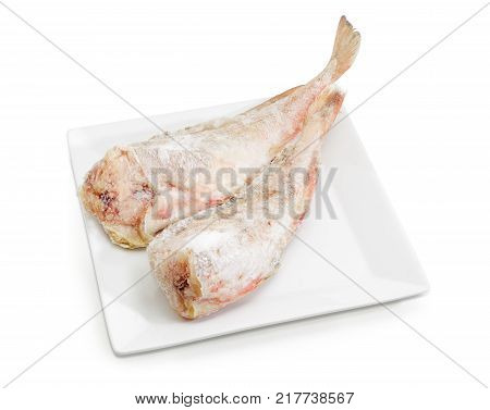 Two carcasses of the frozen red cod without heads on a large square white dish on a white background