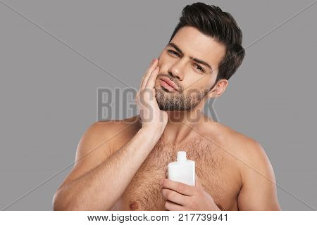 Used to look perfect. Handsome young man applying aftershave lotion and smiling while standing against grey background