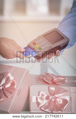 Wireless payment terminal with credit or debit card at shop with gifts in the background 
